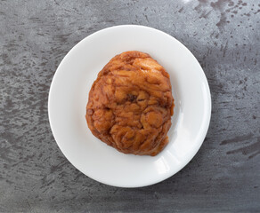 Wall Mural - Top view of an apple fritter on a plate atop a gray tabletop.