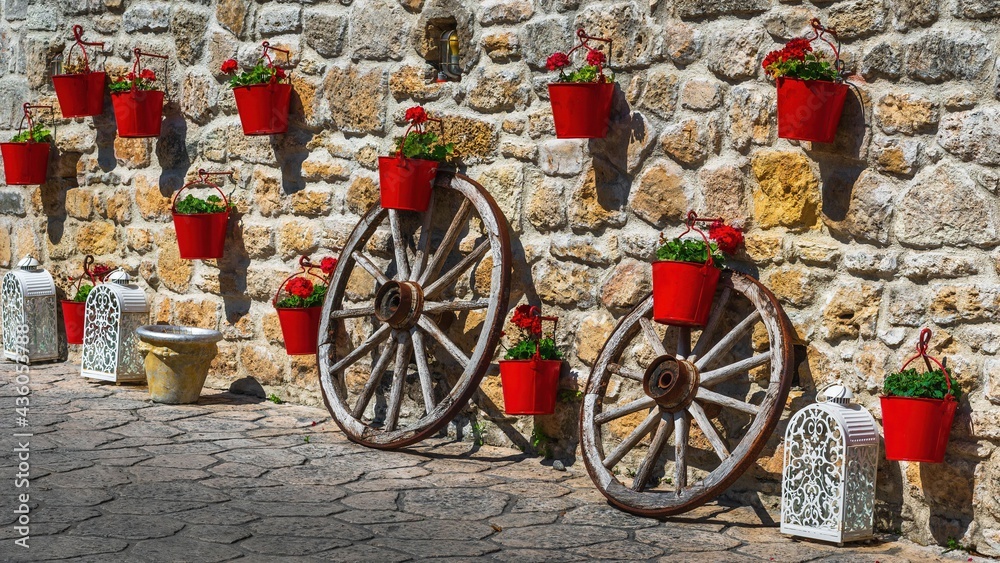 Czerwone doniczki z kwiatami na kamiennym murze w greckim miasteczku - obrazy, fototapety, plakaty 