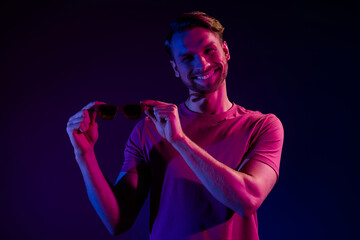 Sticker - Portrait of attractive cheerful successful guy holding specs in hands isolated over dark neon purple color background