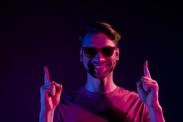 Poster - Portrait of attractive confident cheerful guy demonstrating up copy space advert isolated over dark neon violet color background