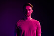 © deagreez - Portrait of attractive serious content guy wearing t-shirt isolated over dark neon light violet color background