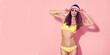 © zamuruev - Beautiful young female in cap, sunglasses and yellow swimsuit looking away while standing on pink background.