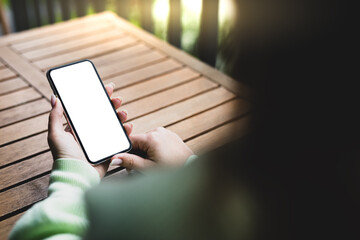 Wall Mural - Girl holding a smartphone with a blank screen on the background of a wooden table in the garden. View from behind the shoulder.