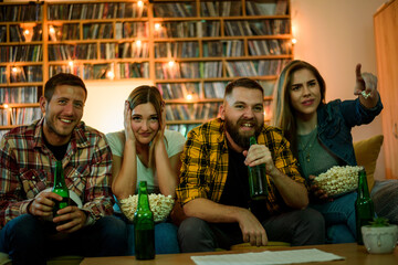 A group of friends watching football game at home and drinking beer