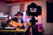 © sofiko14 - Modern digital camera with handsome musician on screen that playing guitar. Young stylish man sitting at studio and recording online lessons about music.