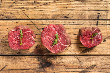 Raw Fillet mignon steaks, beef tenderloin on a wooden butcher table with meat fork. wooden background. Top view