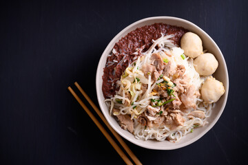 Rice noodle soup with pork, pork ball and vegetables in a bowl and chopsticks on black background, Thai noodles soup