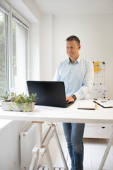 handsome businessman with blue shirt works at high table and is writing something on his black laptop