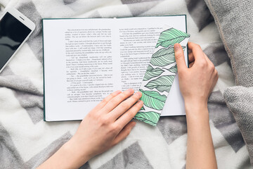 Woman with cute bookmark and book on bed