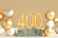 Number 400 On A Concrete Podium And Volumetric Golden Balls On A Beige Background. Copy Space..