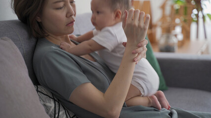 asian woman mother holding heavy baby infant get hurt in wrist and massaging to relieve pain. mother