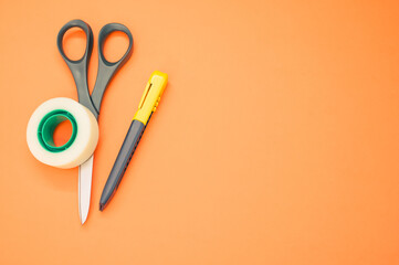 Poster - Closeup shot of scissors adhesive tape and a utility knife on an orange background