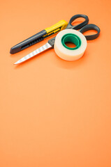 Poster - Closeup shot of scissors adhesive tape and a utility knife on an orange background