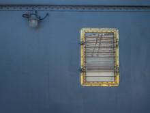 The Metal Wall Of The Ship Is Dark Gray-blue With A Porthole And A Lantern. A Square Porthole In A Gold Frame With A Grille. Reflection Of A City Building In The Glass. Ship's Hull