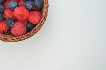 Wall Mural - Top view of fresh raspberries and blueberries in a basket isolated on light gray background