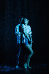 Wall Mural - passionate man gently hugging wet sensual woman in water drops on black background with blue color filter