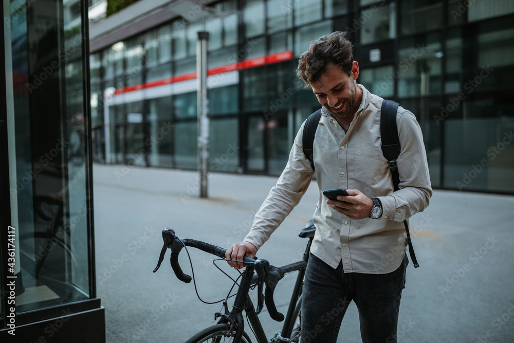 Happy cyclist in the city using phone - obrazy, fototapety, plakaty 