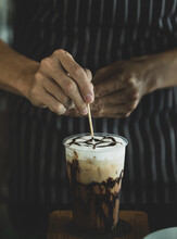 Unrecognizable Barista Carefully Decorating Creamy Foam Of Iced Coffee By Using Toothpick To Draw Chocolate Patterns Onto It Like Spider Net To Make It Look More Attractive To Be Drunk.