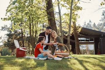 Happy young mother and father with little boy smiling while having picnic outdoors