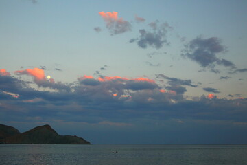 The evening sun lights up the clouds red and the two swim in the sea heads are visible