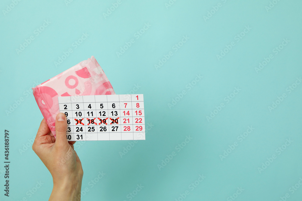 Female hand hold calendar and hygiene pad on blue background - obrazy, fototapety, plakaty 