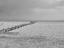 Monochrome Image Of Wooden Pathway Leading Across Stony Beach To Sea