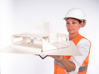 Wall Mural - Woman architect is holding a mock house in front of her. Three-dimensional model of house in hands of architect. Woman examines volumetric layout of cottage. Concept - work of architect.  Planner