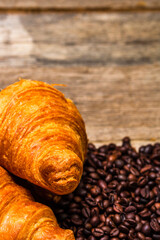 Poster - Freshly baked golden brown French croissant with coffee beans on a wooden surface