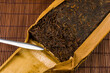 Chinese pressed PU-erh tea in bamboo leaf packaging and tea knife on a bamboo Mat, close-up, macro