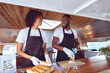 © Wavebreak Media - Smiling diverse couple preparing hot dogs behind counter in food truck