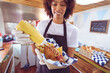 © Wavebreak Media - Smiling mixed race woman pouring mustard on hot dog behind counter in food truck