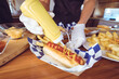 © Wavebreak Media - Midsection of mixed race woman pouring mustard on hot dog behind counter in food truck