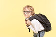 Sad schoolboy with glasses, with a large heavy backpack. Caucasian boy with blond hair on yellow background. Copy space. Concept  of back to school, problems at school, a lot of homework. 