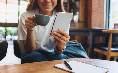 Closeup image of a beautiful young asian woman holding and using mobile phone while drinking coffee