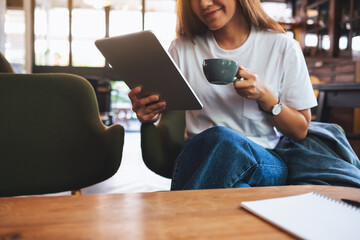 Closeup image of a beautiful young asian woman holding and using digital tablet while drinking coffee