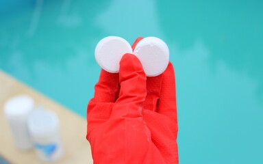 Wall Mural - White mini-tablet of chlorine in the hand of the staff for disinfection of swimming pools. The beginning of the swimming season is hot summer. Rubber protective red glove. Water purification.