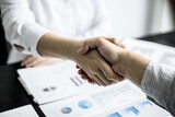 Fototapeta Zachód słońca - A close-up of a person shaking hands, two businessmen shaking hands after agreeing to sign a business investment contract together. The concept of a handshake to show universal reverence.