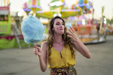 Wall Mural - Attractive young female standing with cotton candy in hand and spending time in an amusement park