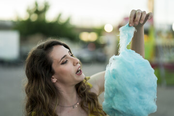 Wall Mural - Attractive young female standing with cotton candy in hand and spending time in an amusement park