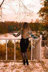 Wall Mural - Smiling youth stands leaning against a white railing an adult blonde with gentle lips, in a colored shirt, standing against the background of the steps laughing autumn real people dark mask blue eyes