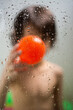 Vertical shot of a boy in the shower holding a plastic ball behind glass with drops