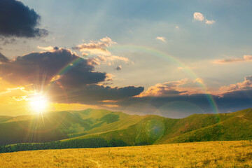 mountain landscape in summer at sunset. grassy meadows on the hills rolling in to the distant peak beneath a rainbow in evening light