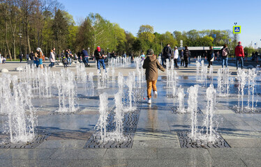 Children have fun and play with the water jets in the fountain on a warm summer day.