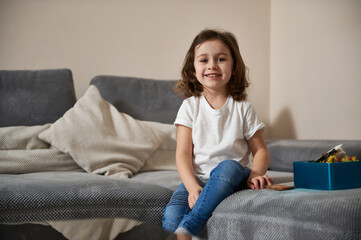 Portrait of adorable preschool girl in casual clothes sitting on a sofa in the living room