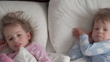 Authentic Caucasian 2 Little Siblings Preschool Baby Girl Boy In Pink Blue Sleepy Upon Waking Looking At Camera Smiling Cute And Grimaces In White Bed. Child Care, Childhood, Parenthood, Life Concept