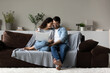 © fizkes - Happy millennial multiethnic man and woman relax on couch at home using laptop together. Smiling young multiracial couple rest on sofa in living room have fun browsing internet on computer.