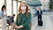 © VAKSMANV - Camera approaching young pretty Caucasian positive woman standing with passport in city looking at camera at bus station. Close up of pretty female in mask travelling, coronavirus, covid pandemic