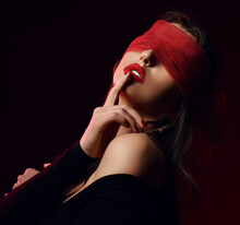 Portrait Of Sexy Brunette Pretty Woman Model In Black Clothes And Red Transparent Mask On Eyes Touching Lips Over Dark Background. Stylish Look And Sexual Games Concept