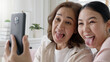 © ChayTee - Attractive beautiful two people asia young lady girl use mobile phone take photo picture video camera overjoy sit at home sofa couch have good time day together quarantine in mum healthy health care.