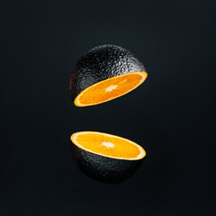 Wall Mural - Orange painted on black and cut in half levitating against black background. Creative food concept. Unique and unusual fruit composition.